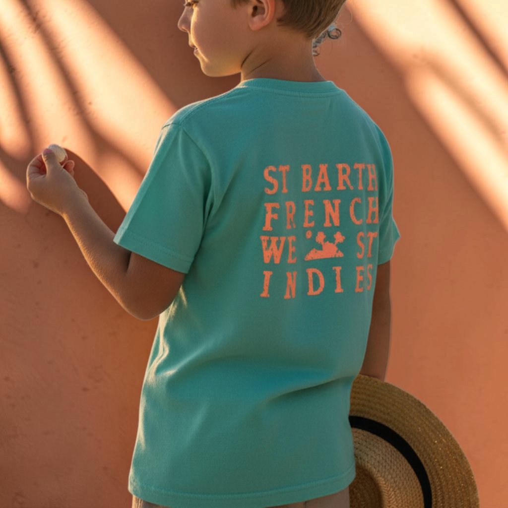 Enfant portant un t-shirt vert d'eau St Barth French West Indies avec logo orange au dos, tenant un chapeau de paille