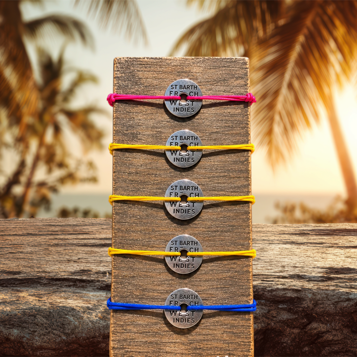 Bracelets St Barth French West Indies avec jetons en mΓ©tal gravΓ© et cordons Γ©lastiques colorΓ©s sur un socle en bois