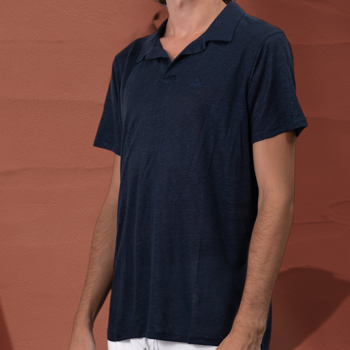 Homme portant un polo en lin bleu marine St Barth French West Indies avec un short blanc sur fond neutre