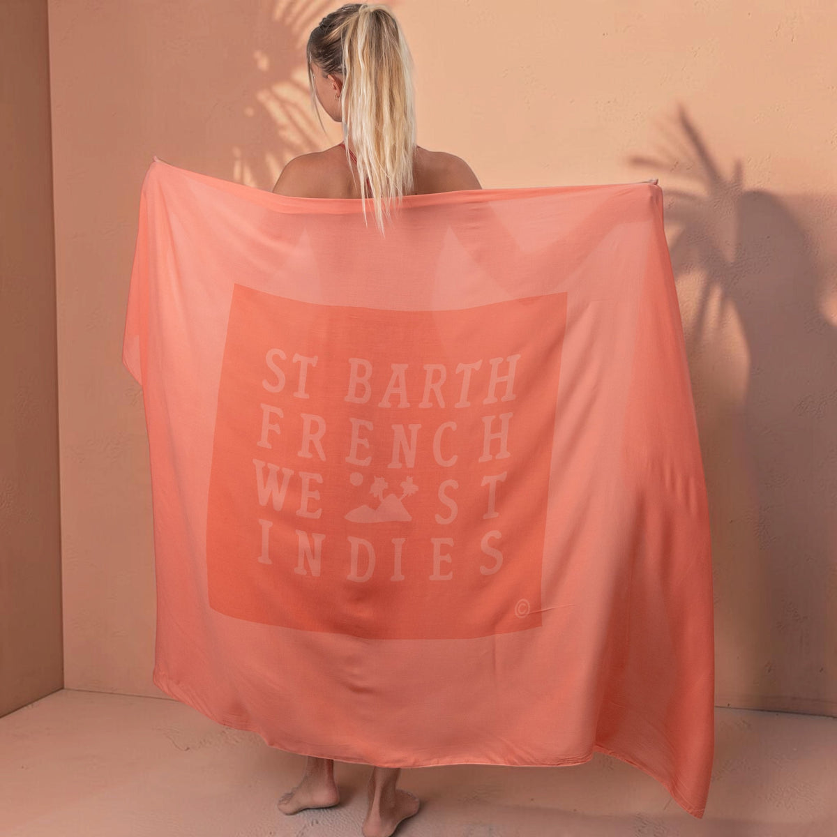 Femme tenant un paréo St Barth French West Indies en voile de rayonne corail doux avec logo imprimé
