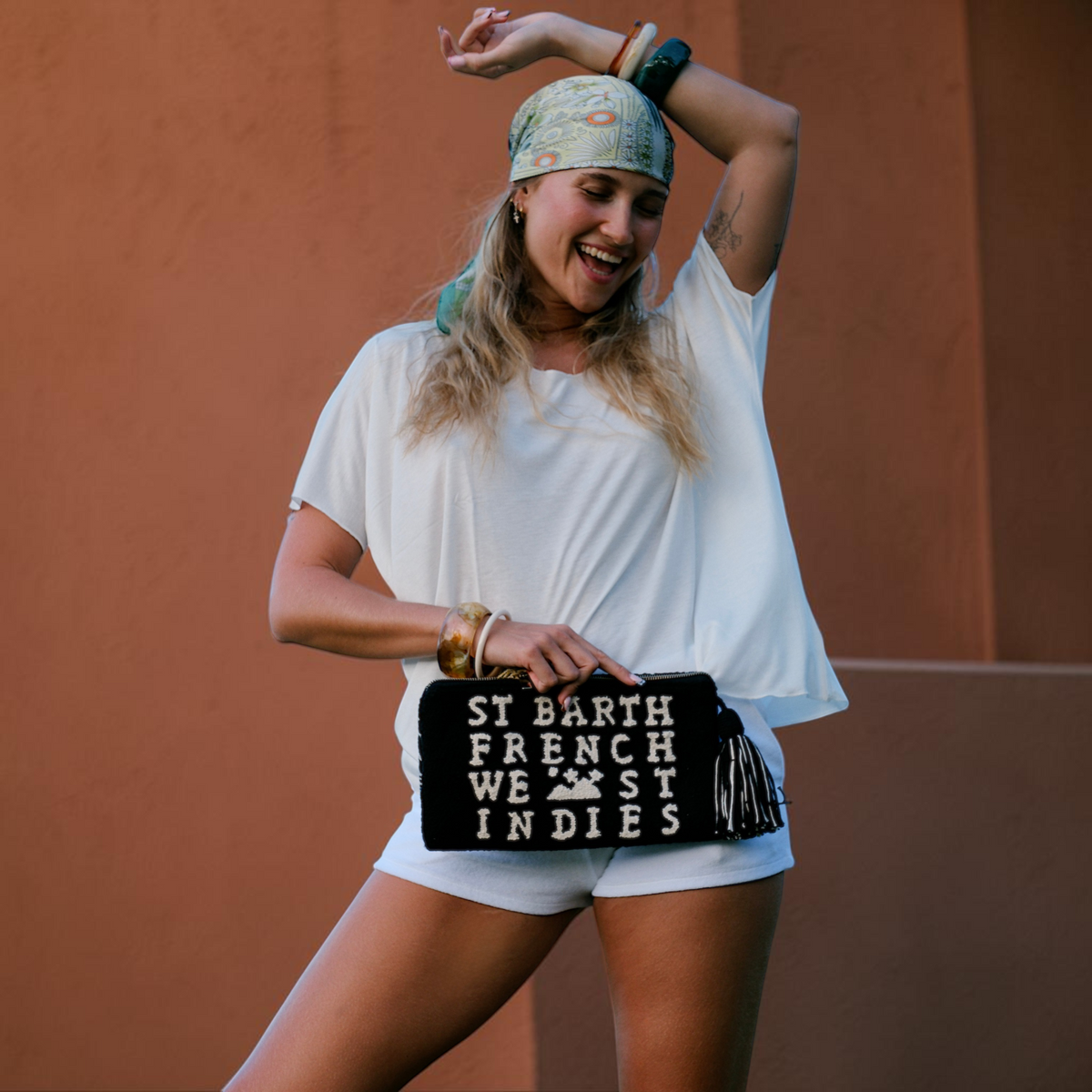 Femme souriante portant une pochette artisanale noire St Barth French West Indies avec broderies blanches