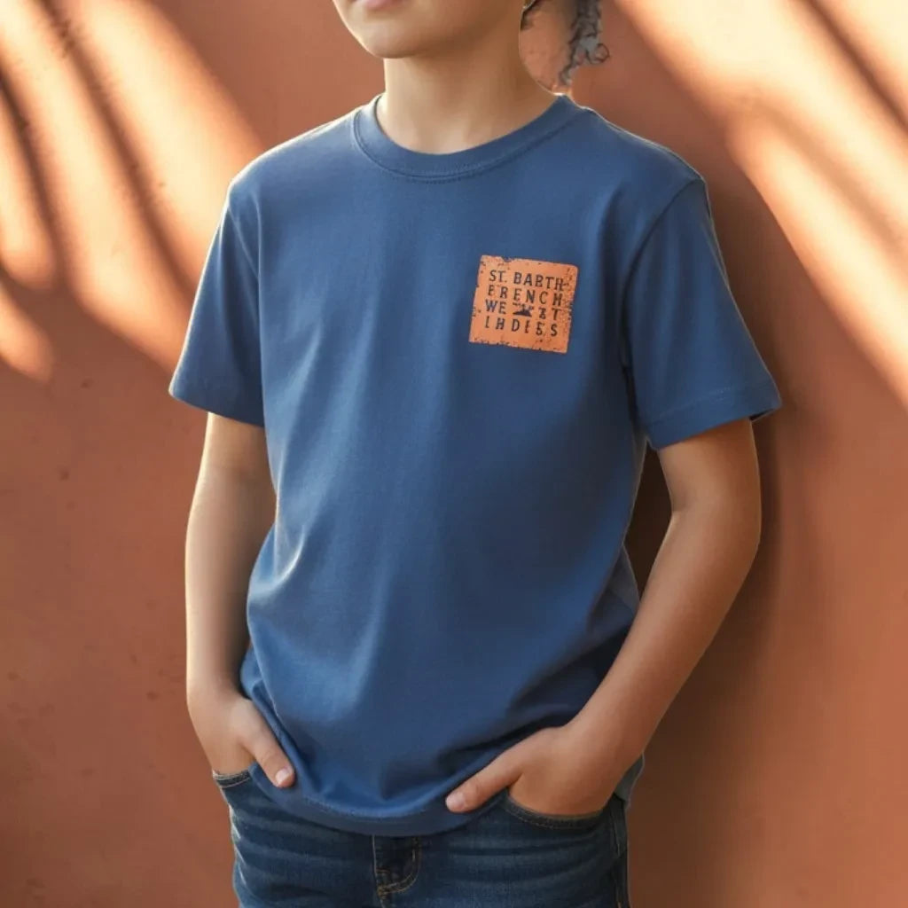 Enfant portant un t-shirt bleu St Barth French West Indies avec un logo carré orange sur la poitrine