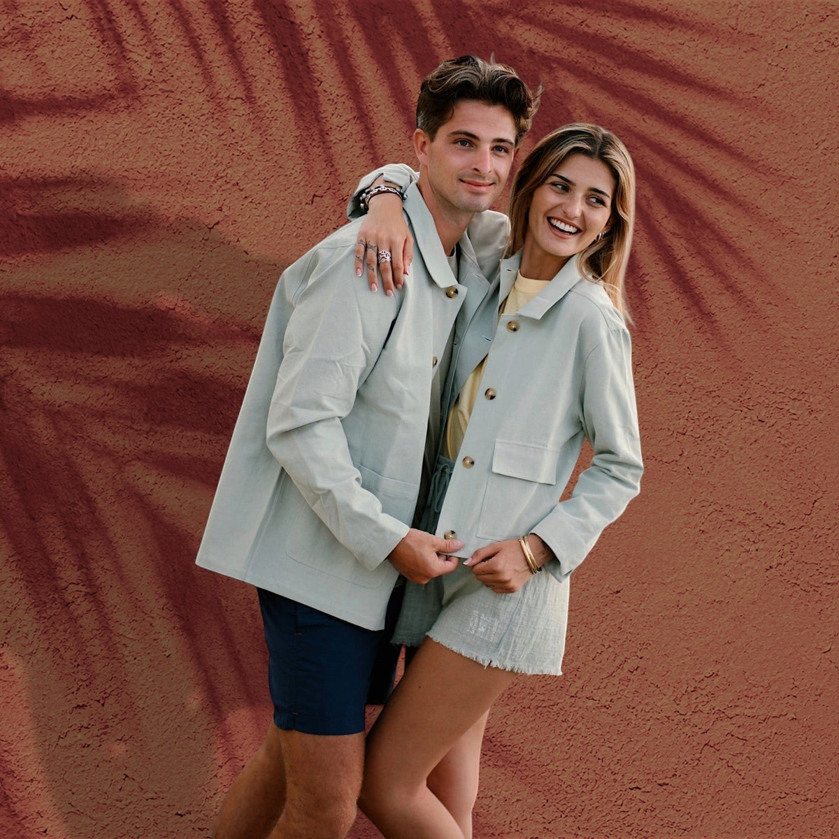 Couple portant la veste chemise ROMY vert sauge de St Barth French West Indies devant un mur texturé terracotta