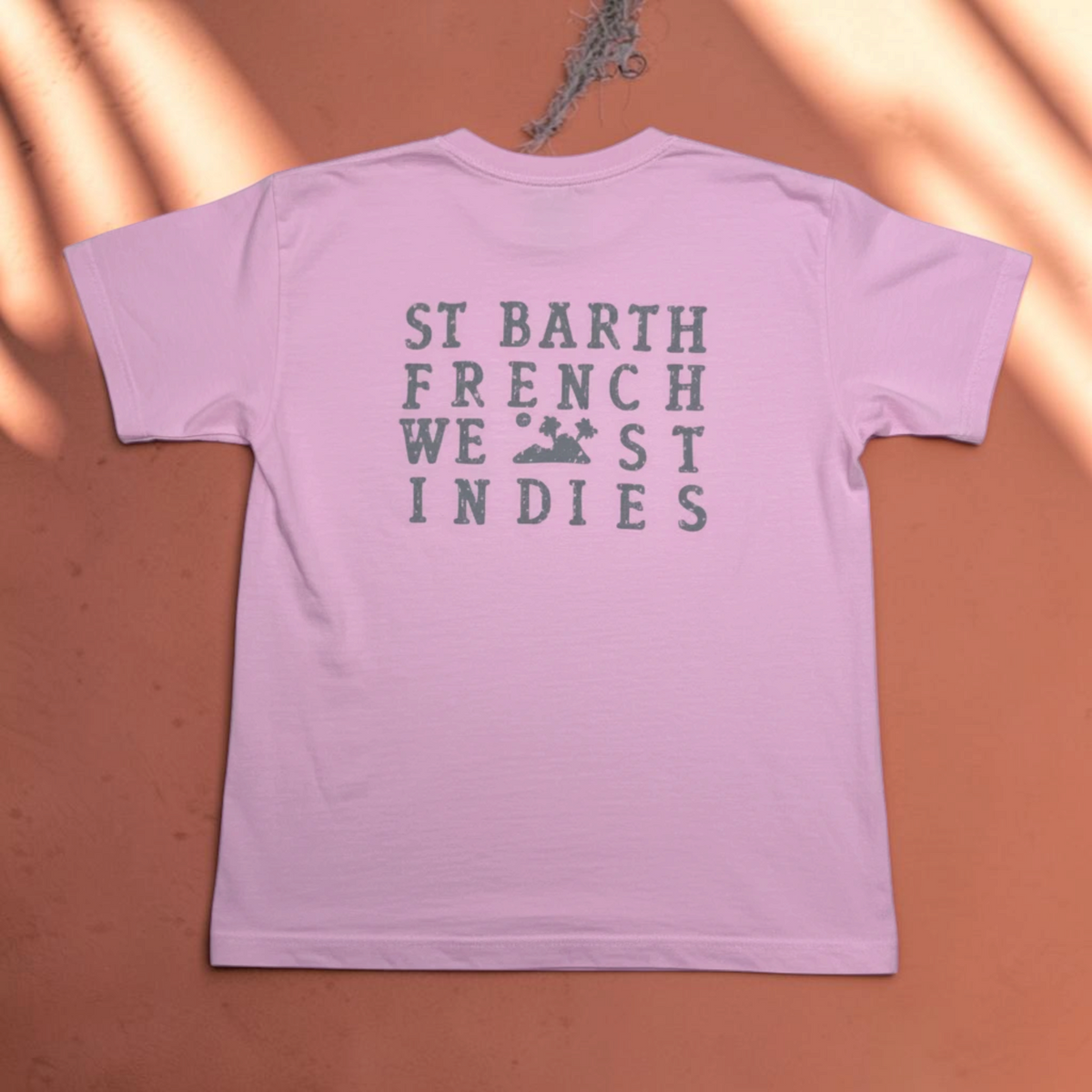 T-shirt rose pour enfant St Barth French West Indies avec logo imprimé au dos sur cintre en bois