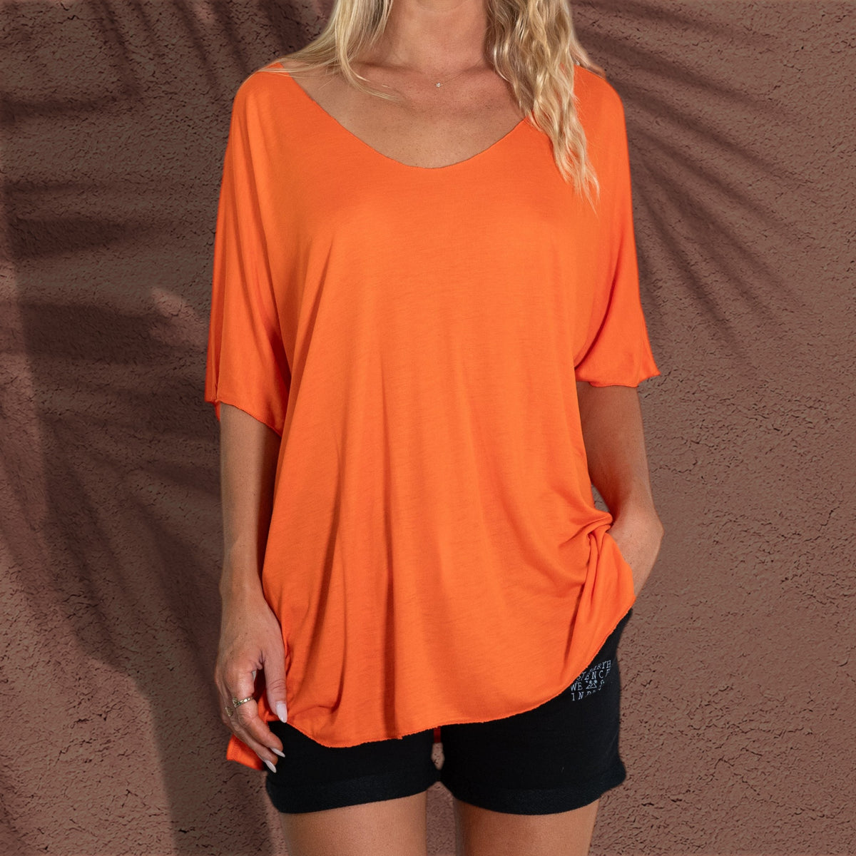 T-shirt Batgirl St Barth French West Indies orange en viscose avec manches ailes porté sur des shorts noirs