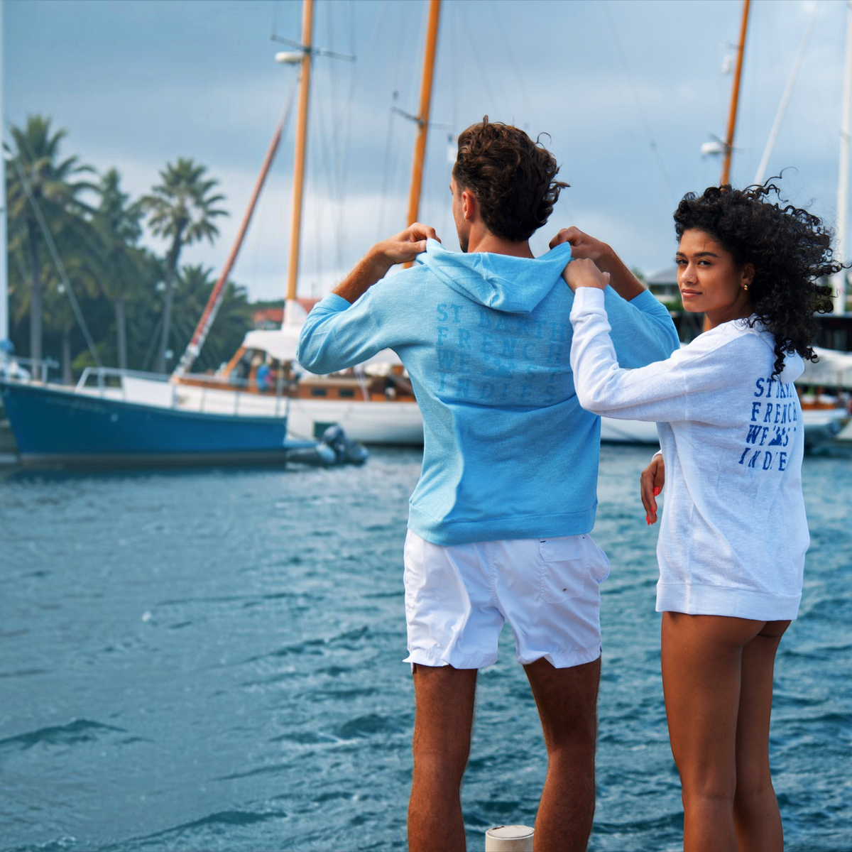Couple portant des sweats à capuche St Barth French West Indies en coton bleu et blanc au bord d'un port de plaisance