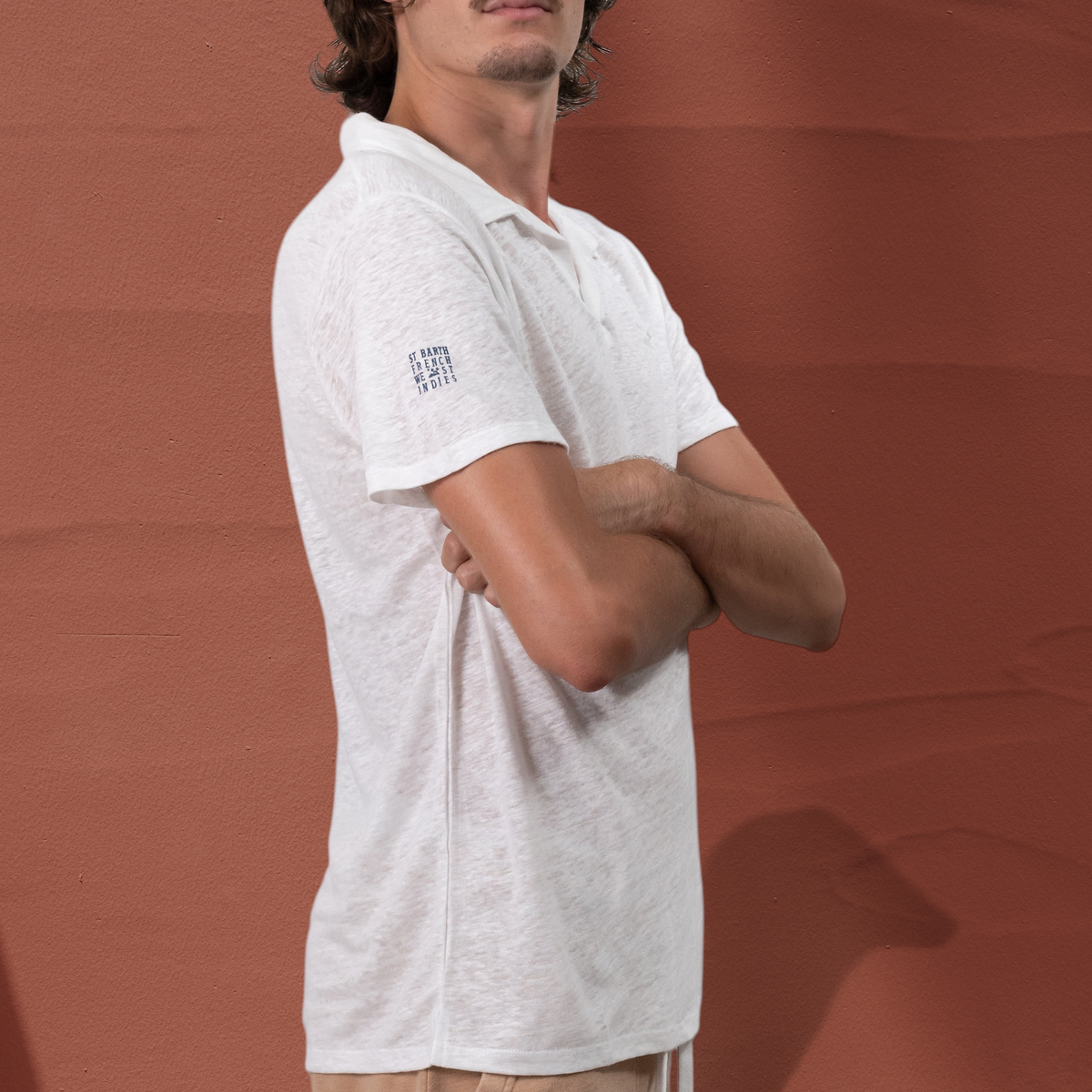 Homme portant un polo en lin blanc St Barth French West Indies avec logo imprimé sur la manche, vue de profil