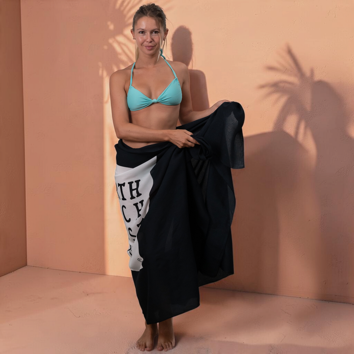 Femme portant un paréo St Barth French West Indies en voile de rayonne noir avec logo blanc, style plage