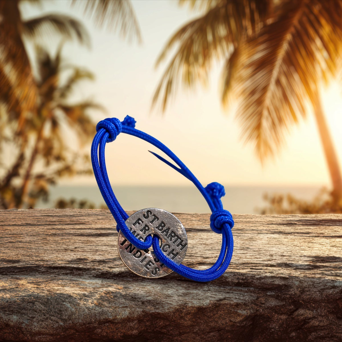 Bracelet élastique bleu St Barth French West Indies avec une pièce métallique gravée sur un bois flotté au coucher