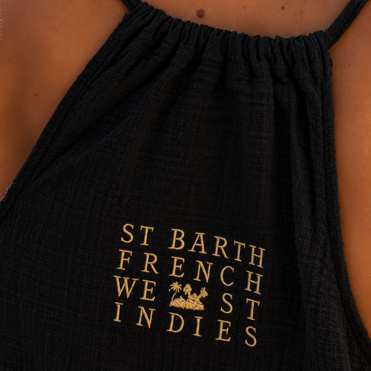 Gros plan sur la broderie dorée du logo St Barth French West Indies au dos d'une robe Alice en gaze de coton noire.