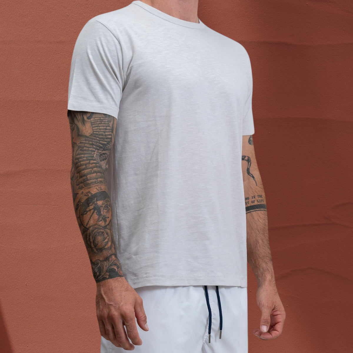 T-shirt Jasper St Barth French West Indies en coton slub gris clair porté par un homme tatoué sur fond orangé