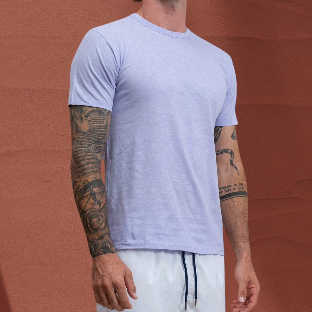 Homme portant un t-shirt St Barth French West Indies Jasper en coton slub lilas clair devant un mur orange